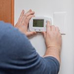 A man is examining how to fix air conditioner thermostat at home.