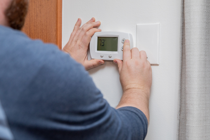 A man is examining how to fix air conditioner thermostat at home.