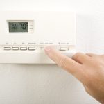 A man is adjusting his thermostat settings because the air conditioner not heating properly.