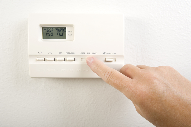 A man is adjusting his thermostat settings because the air conditioner not heating properly.