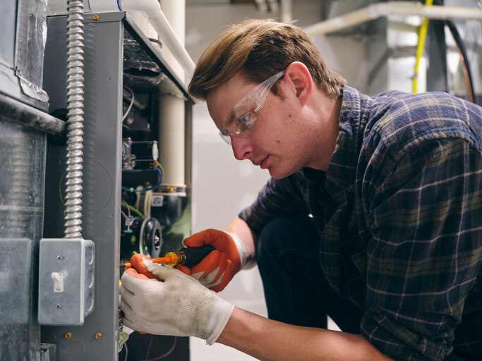 Professional HVAC technician inspecting a furnace control board to determine how much furnace repair will cost for a homeowner.